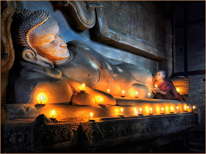 Monk praying at foot of reclining Buddah